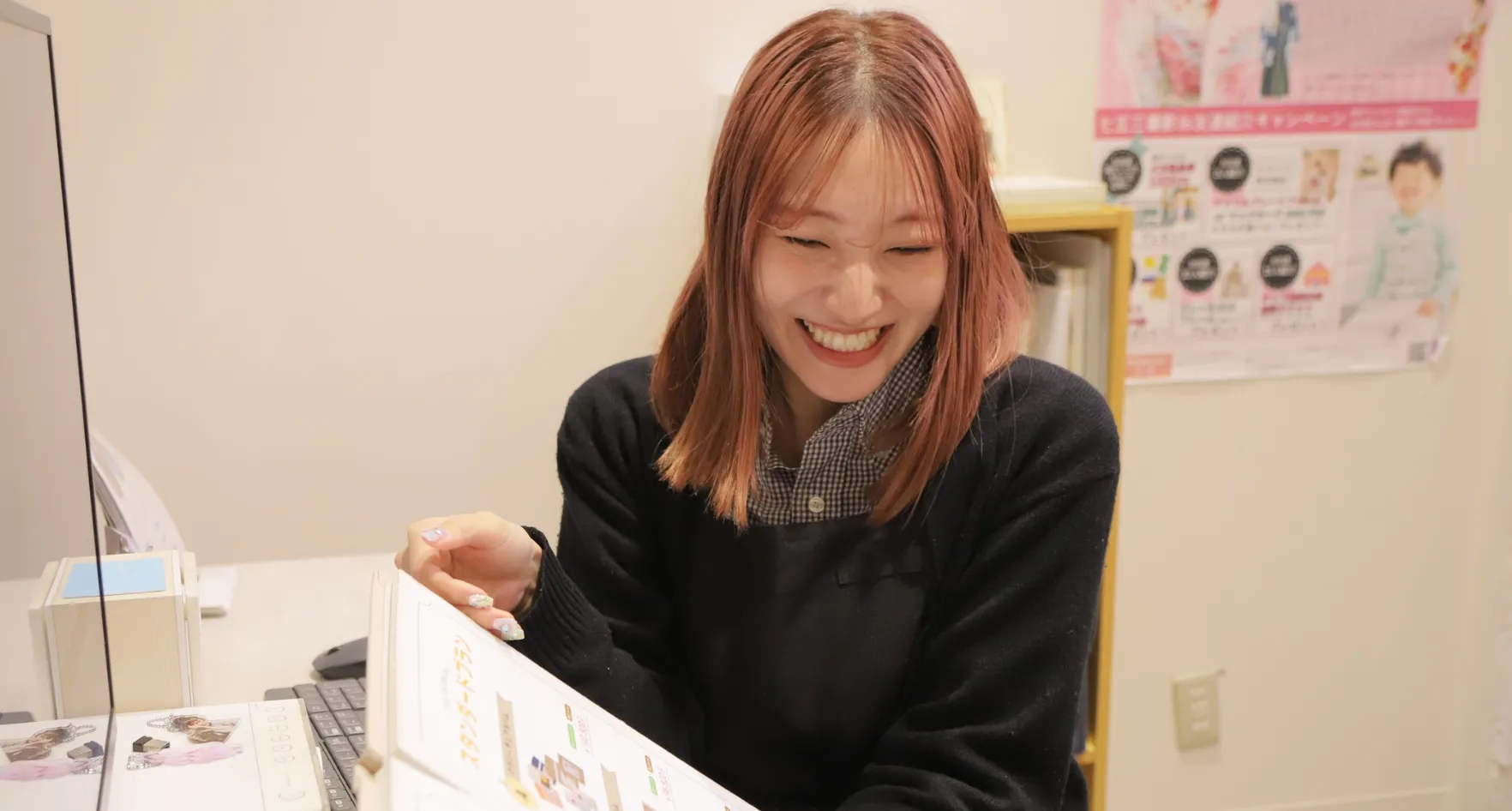 美容部Hさんのインタビュー写真（資料を見ながら笑顔）